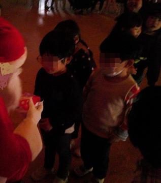 暗い室内で幼児がサンタさんからプレゼントを受け取っている様子