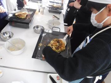 鉄板のお好み焼きをひっくり返す児童たちの様子