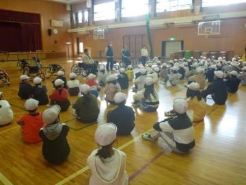 4年生が体育館で車いすバスケットの説明を聞いている。