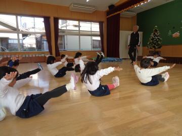 体操教室に参加し床に座って手を広げ、足を延ばして足を上に上げ、動きを止める飛行機のポーズをしている