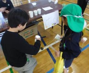 けん玉ブースで生徒が園児にけん玉を実演して教えるようす