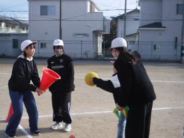 赤い三角コーンの角を下に向けて持つ児童の三角コーンの中にボールを投げ入れようとする児童