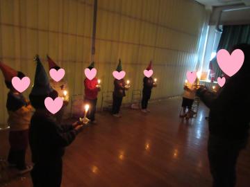 照明を落とした室内でキャンドルサービスをする児童たちの様子