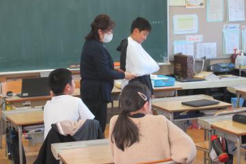 先生が三角巾を使って応急手当の手本を示している様子