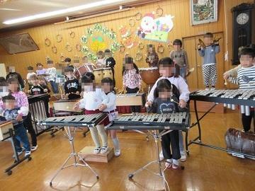 5歳児が楽器遊びを3、4歳児に教えている写真