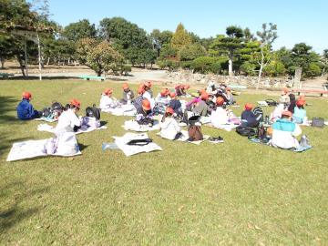 芝生の上でレジャーシートを敷いて、その上に座ってお弁当を食べている子供たち