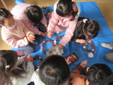 室内の床で集まってリースを作る幼児の様子