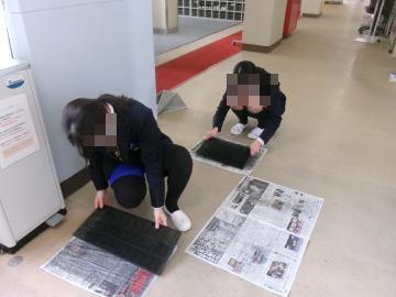 生徒二人が廊下でエアコンフィルターの掃除をしています。