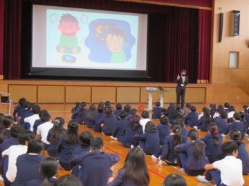体育館で全校生徒が整列して座り、規則正しい生活についての話を先生から聞くようす
