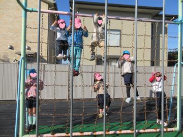 園庭で園児たちが登り棒で遊んでいる様子