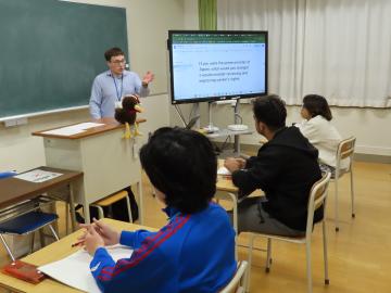 教室で着席している生徒からの質問に答えるルイス先生のようす