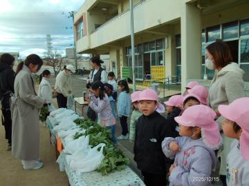 園庭で保護者がお客になって子供たちのお店屋さんで野菜を買う様子