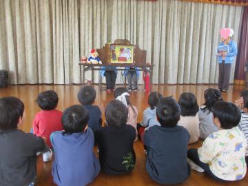 遊戯室内で座って紙芝居を見る子供たち