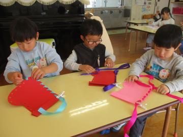 室内で画用紙で作ったブーツの穴にひもを通す子供たち