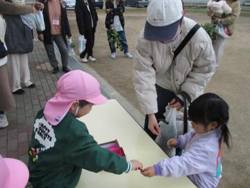 園庭で野菜を買った保護者から紙で作ったお金を受け取る子供
