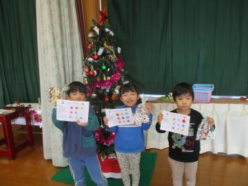 遊戯室内でツリーの前で手作りのビンゴカードとお菓子を持ってうつる子供たち