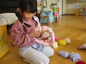 室内で輪っかに毛糸を巻いてリースを作る子供