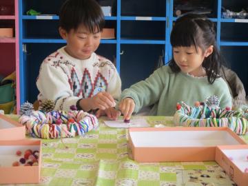 室内で毛糸のリーズに飾りを付ける子供たち