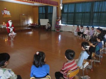 遊戯室内でサンタクロースを囲む子供たち
