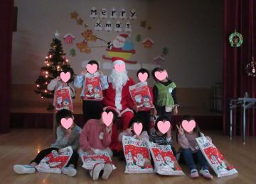 遊戯室内で園児たちがサンタさんと集合写真を撮っている様子