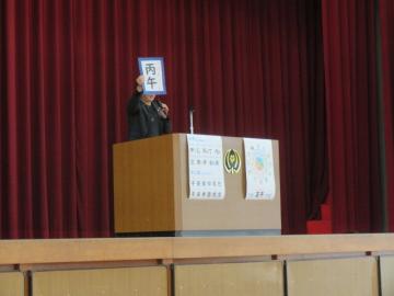 体育館の壇上で干支の説明をする校長の様子