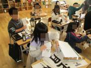 教室の自分の席で書初めをする3年生