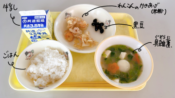 給食の写真です。牛乳、ごはん、れんこんのかきあげ、黒豆、お雑煮がお盆の上に並んでいます。