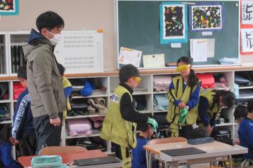 教室内で3年生がゴーグル、チョッキ、手袋などを装着している様子