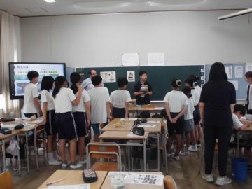 教室の黒板側に立っている埋蔵センターの職員が持つ発掘された壺に近づいて見学する生徒達