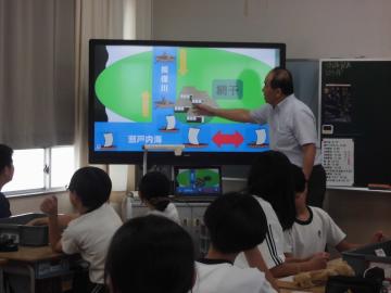 鎌倉時代の魚吹神社の貿易について表示されているディスプレイをさして説明する教師とそれを自席に座って聞く生徒たち