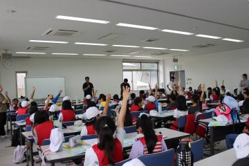 3年生が坊勢漁協の会議室で、今日見たことや調べたことに対する質問のために挙手をする様子