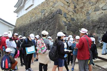 6年生が姫路城を間近に見える場所でガイドさんに石垣について説明してもらっている様子