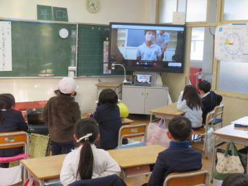 教室で席に座った1年生がテレビ画面に映る先生クイズに答えるようす