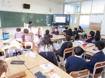 教室で席に座った2年生がテレビ画面に映る先生クイズに答えるようす