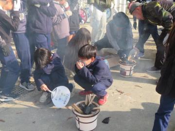 校庭で長寿会の方に教えていただき七輪で火おこしをする3年生と4年生の児童たちの様子