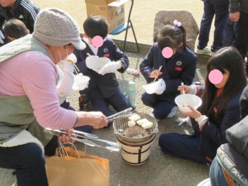 校庭で長寿会の方と一緒に七輪でもちを焼く3年生の別の児童たちの様子