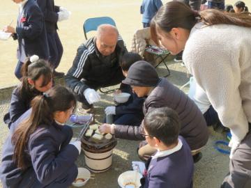 校庭で長寿会の方と一緒に七輪でもちを焼くさらに別の3年の児童たちの様子