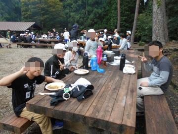 5年生が外にある木のテーブルで、自分たちが作った昼食をみんなで食べる様子