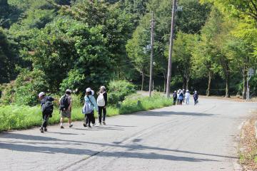 5年生がスタンプラリーで班別に広い山の道路を移動する様子