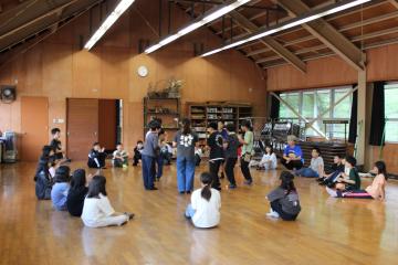 5年生が体育館で輪になって座る生徒と、その中心で立つ生徒に分かれてスタンツ練習をしている様子