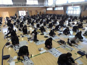 体育館にて一斉に書初めをする生徒たちの様子