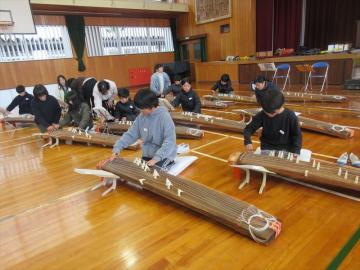体育館の床に置かれたお箏で演奏の体験をする児童たちの様子
