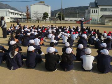 校庭で体操座りし、避難訓練についての講評を聞く児童たちの様子