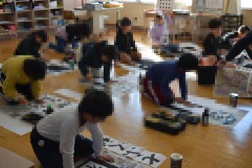 教室内で床に置かれた用紙に筆で書初めをする児童たちの様子