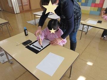 地域の方に書初めの指導をしてもらうこどもの様子