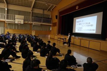 体育館で講師が立って震災学習の説明をしているのを一生懸命聞く生徒の様子