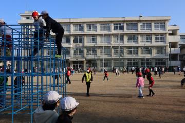 校庭に散らばった生徒たちが遊んでいたり、写真手前の青いジャングルジムに生徒数名がのぼっていたりする写真