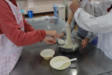 ひまわり学級の子どもたちが調理実習室でつっくているおもちを手と棒で伸ばしている写真