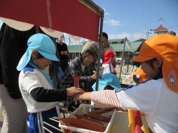 園庭で保護者と模擬の売り買いを楽しむ園児たちの様子