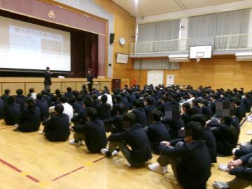 全校生徒が体育館の舞台前に全校集会の隊形に並んで座り、舞台前で講師の先生に生徒会役員がお礼の言葉を述べています。